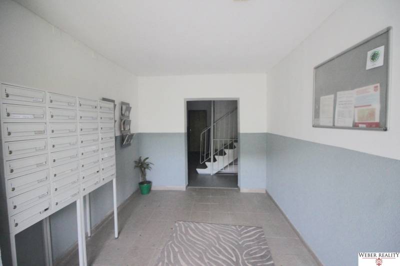 The entrance hall of an apartment building with a staircase, mailboxes, and a bulletin board.