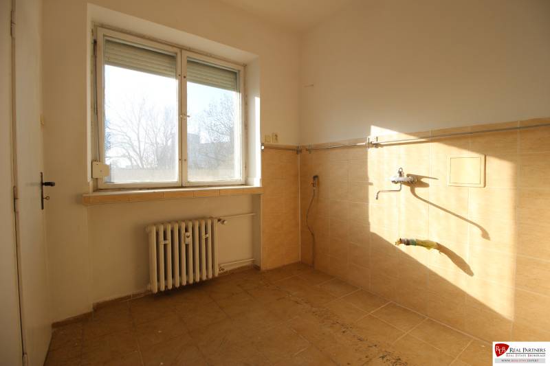 An empty kitchen with a window in a 3-room apartment, unfurnished, light tiles.