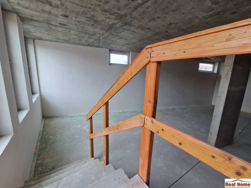 Unfinished interior of a gastro space with a staircase and a concrete ceiling.