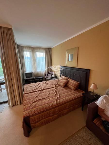 A bedroom with a bed and a TV in a holiday apartment, bright curtains.