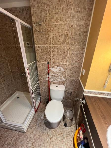 A bathroom in a holiday apartment with a toilet, shower, and part of a sink.