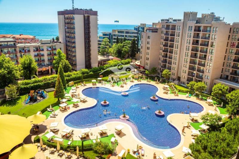 A holiday apartment on the Sunny Beach with a pool surrounded by modern buildings and a sea view.