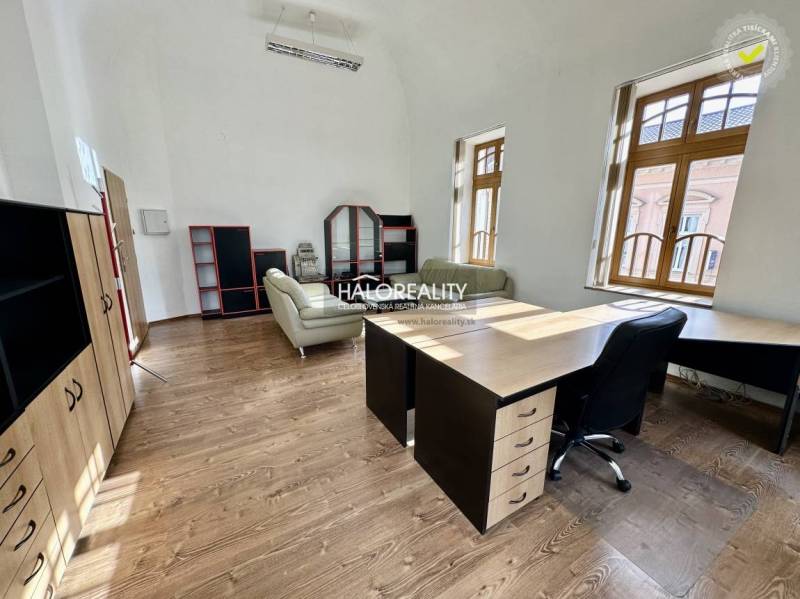 Office with wooden flooring, leather chair, and large windows, bright interior.