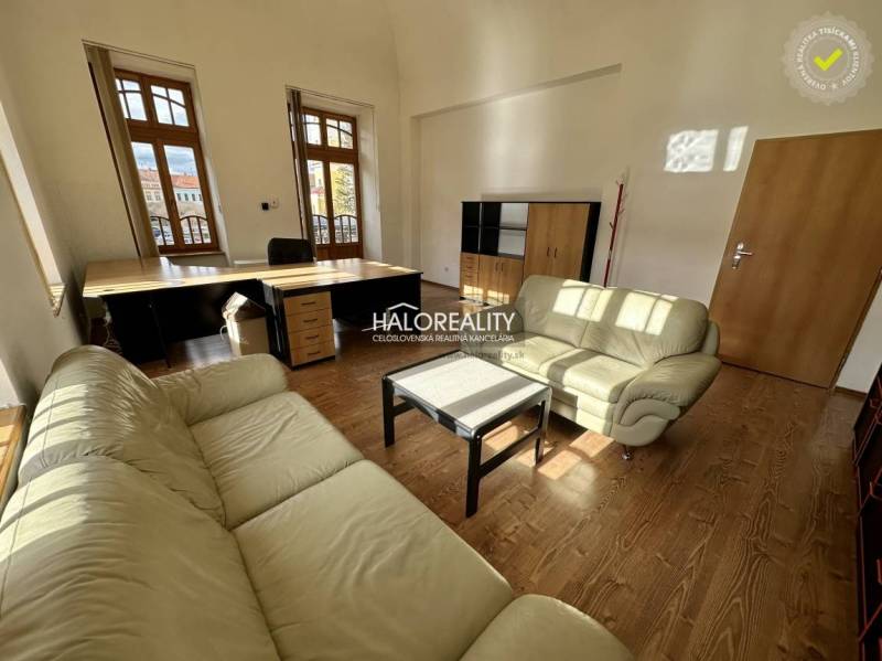 An office interior with leather sofas, wooden flooring, and large windows.