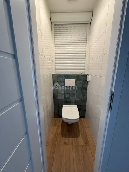 A bathroom in a 2-room apartment with a wooden floor and a tiled wall.