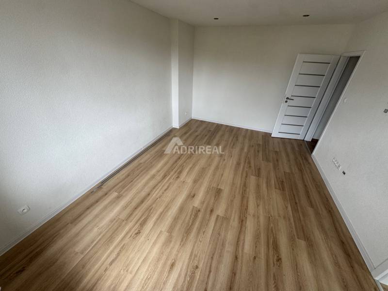 An empty room with wooden flooring and white walls in a 2-bedroom apartment.