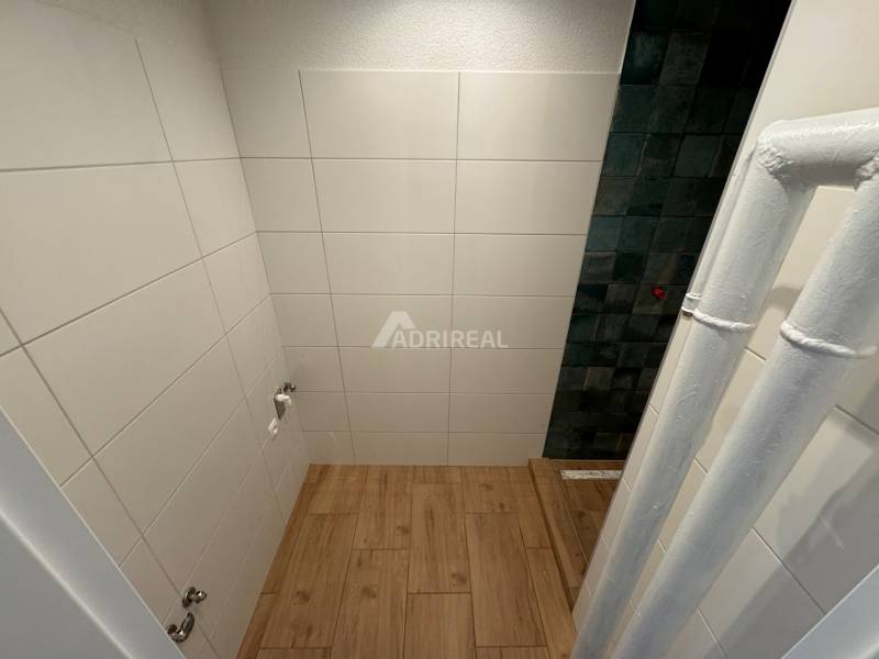 A bathroom with ceramic tiles and wooden flooring in a 2-room apartment.
