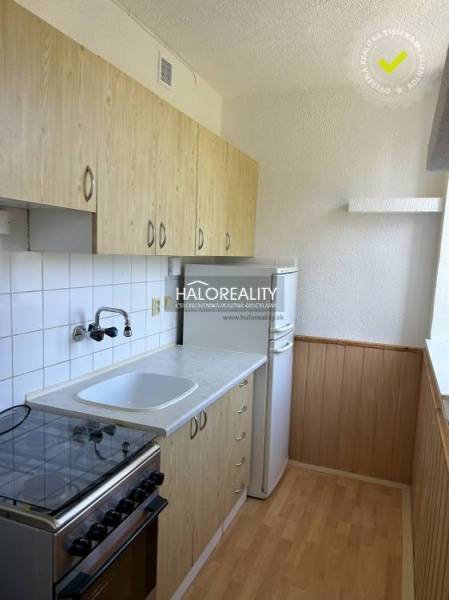 A kitchen in a studio apartment with wooden cabinets, a stove, and a white refrigerator.