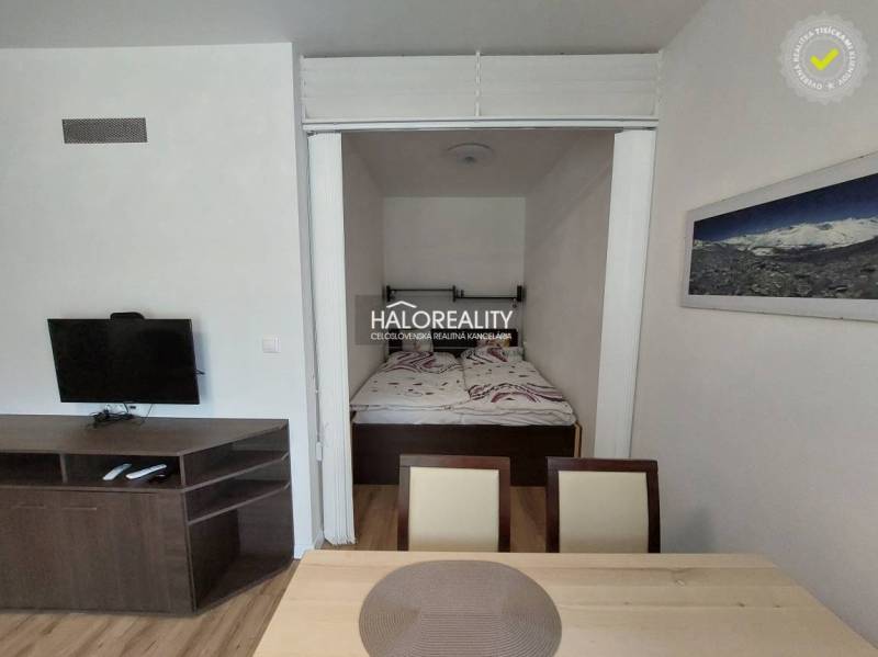 Interior of a 1-room apartment with a television, double bed, and dining table.