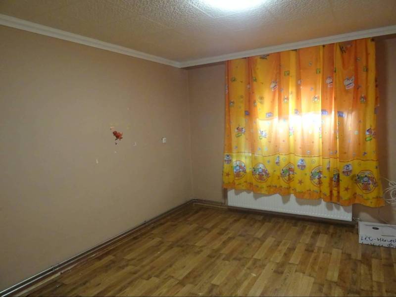 A room in a family house with a wooden floor and orange curtains with a children's motif.