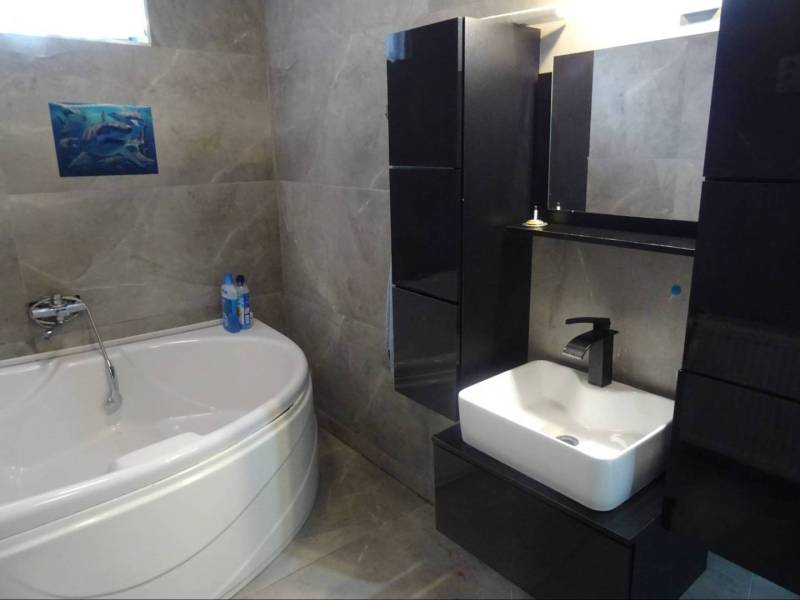 A bathroom in a family house with a corner bathtub and black cabinets.