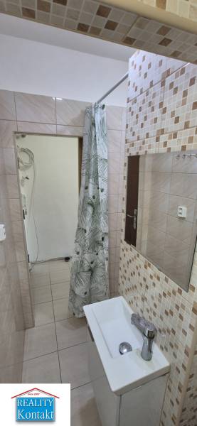 A bathroom in a studio apartment with a sink, shower, and tiles in beige tones.