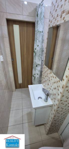 A bathroom in a studio apartment with a sink and a shower curtain, light tiles.