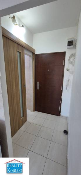 Entrance hallway in a one-room apartment, wooden door, white walls, and tiles.