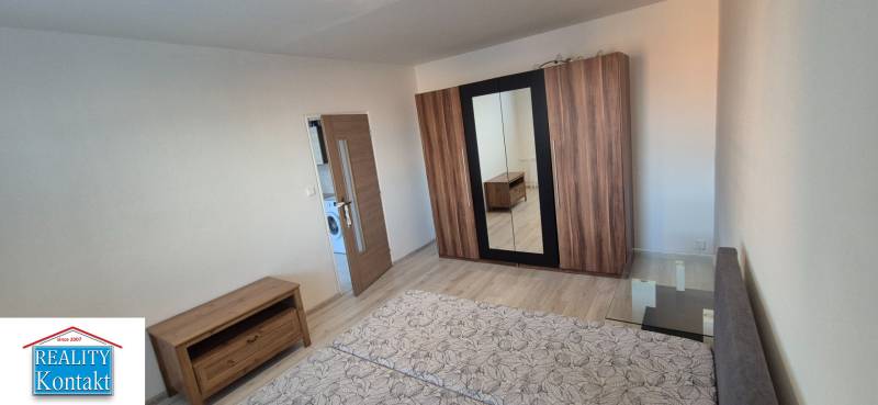A bright room with a double bed, a wardrobe, and wooden furniture in a studio apartment.