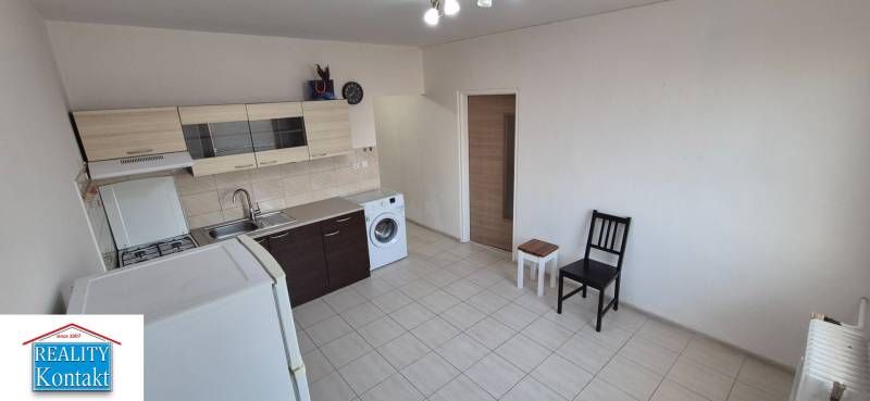 A kitchen in a studio apartment with furniture, a washing machine, and a refrigerator.