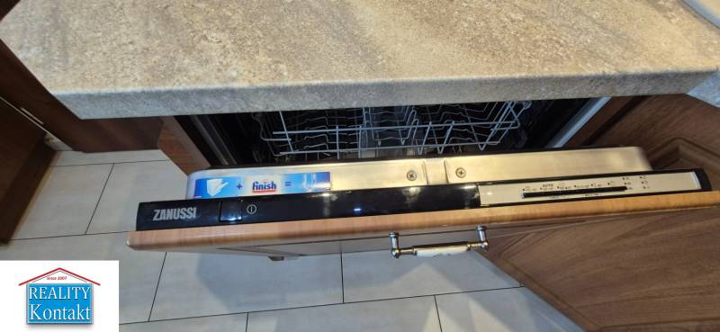 An open Zanussi dishwasher in a studio apartment with a wooden kitchen interior.
