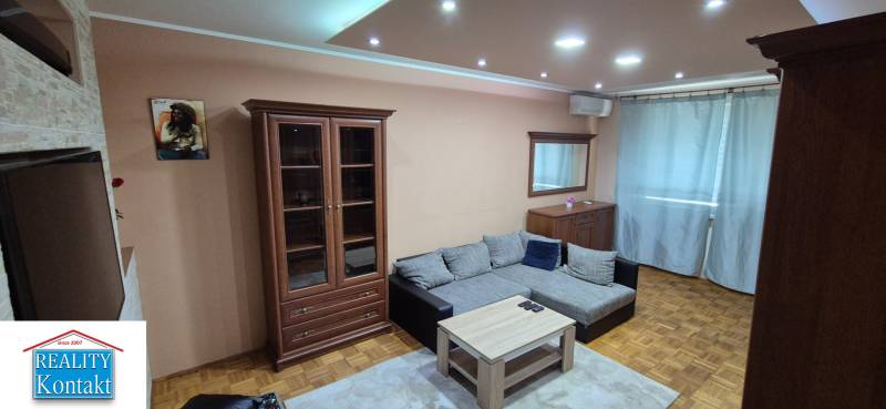 Living room in a studio apartment with a sofa and wooden furniture, illuminated by spotlights.