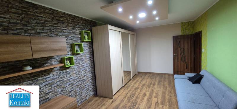 Living area of a studio apartment with a stone wall, mirrored wardrobe, and sofa.