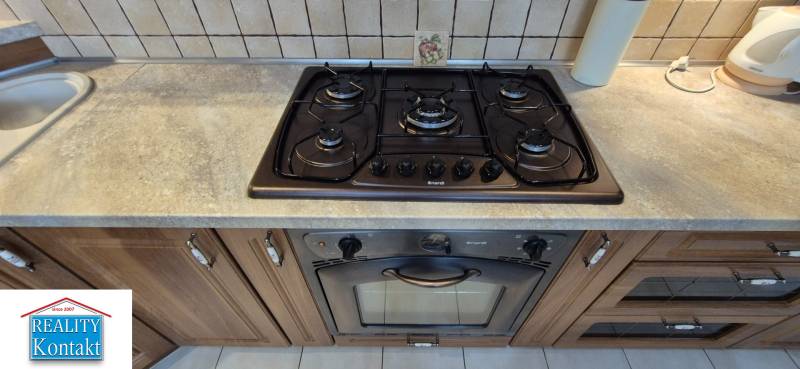 A kitchen with a gas stove and oven in a studio apartment, wooden cabinets, and tiled backsplash.