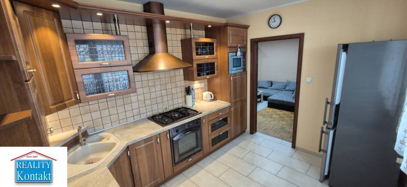 A kitchen in a studio apartment with wooden cabinets, a range hood, and built-in appliances.