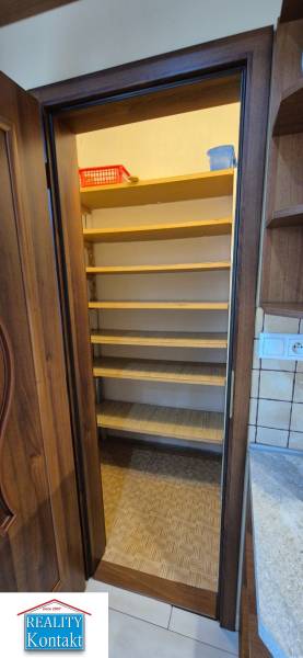 A pantry with shelves in a one-room apartment with a wooden door frame and tiles.