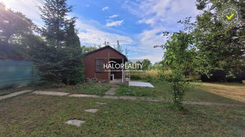 A garden in Nitra with a wooden cottage, surrounded by trees and green grass.