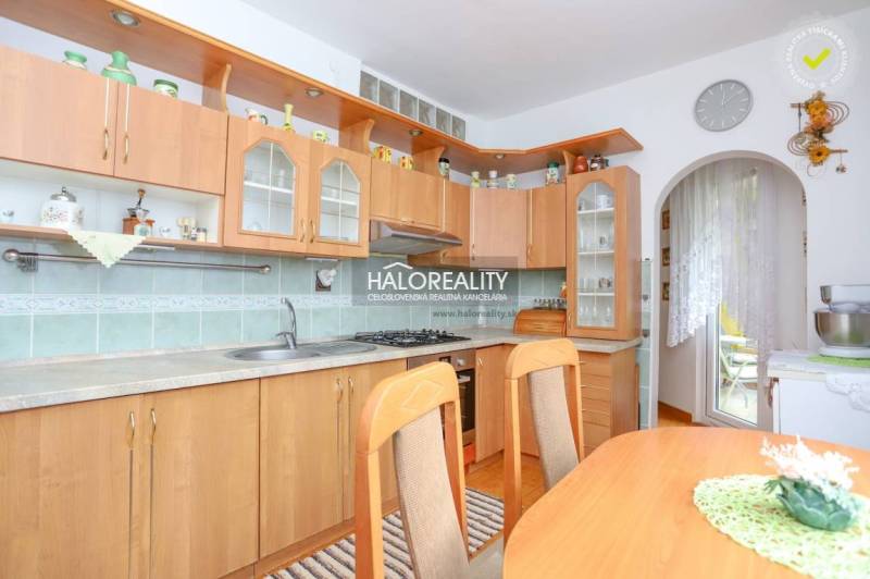 A kitchen in a 3-room apartment with a wooden cabinet, a dining table, and access to the balcony.