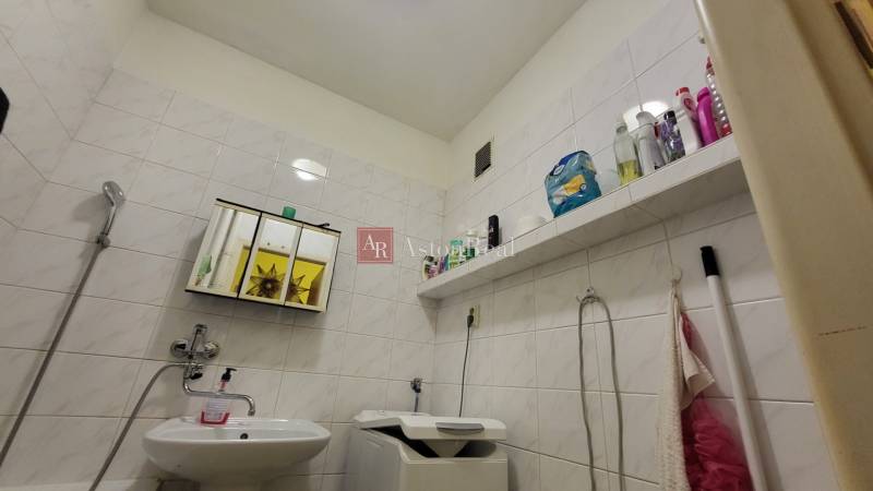 A bathroom in a 3-room apartment with a washing machine, a sink, and storage space for hygiene products.
