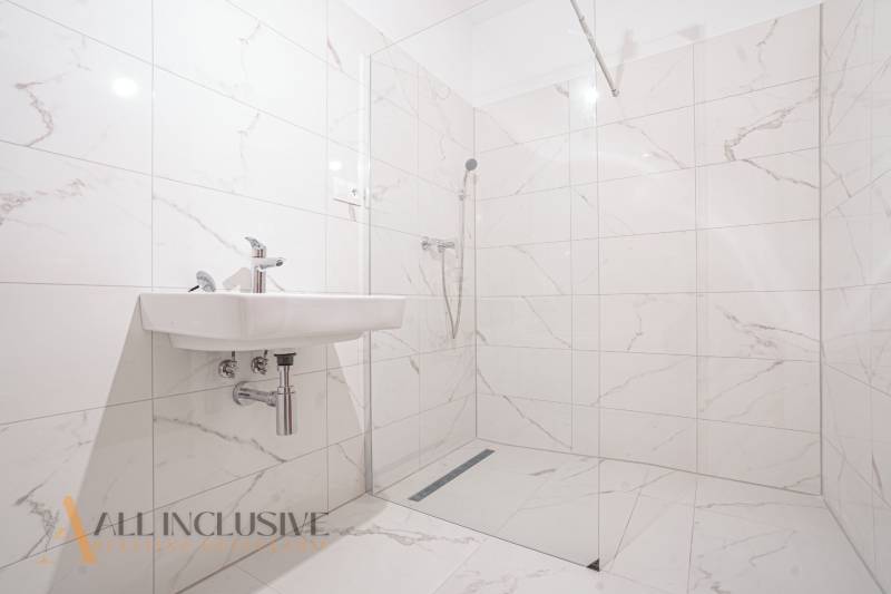 A bathroom in a family house with a sink and a shower, featuring predominantly white tiles.