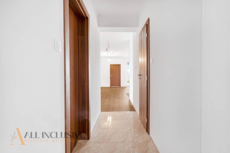 A hallway in a family house with white walls, wooden doors, and tiled flooring.