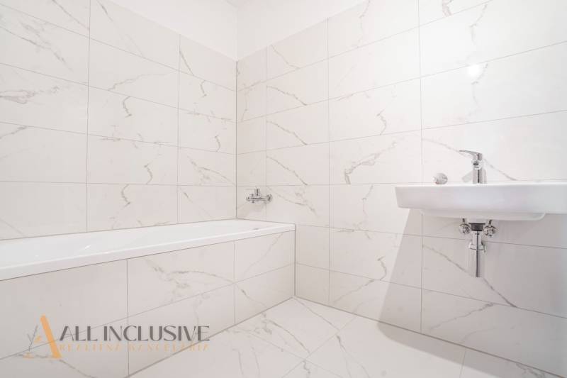 A bathroom with a bathtub and a sink in a family house, tiled with light ceramic tiles.