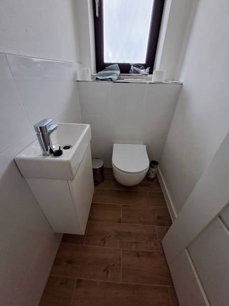 A small bathroom with a sink and toilet in a family house, complemented by a wooden floor.