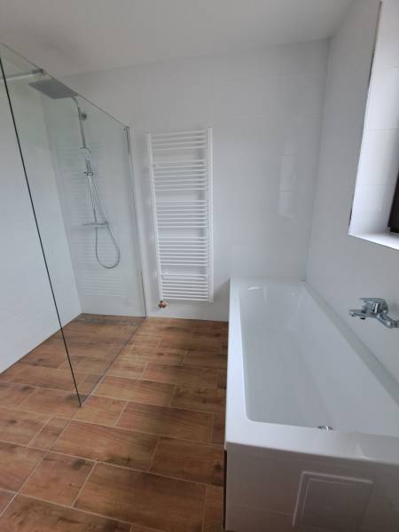 Bathroom in a family house with a bathtub and a shower, wooden tiles on the floor.