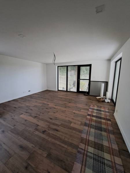 A room in a family house with a wooden floor and large windows with blinds.