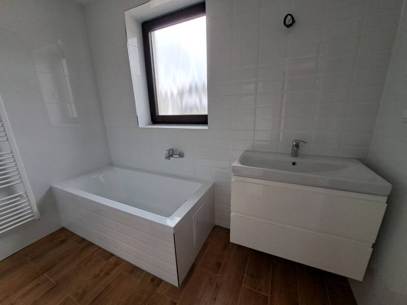 A bathroom in a family house with a bathtub and a sink on a wooden floor.