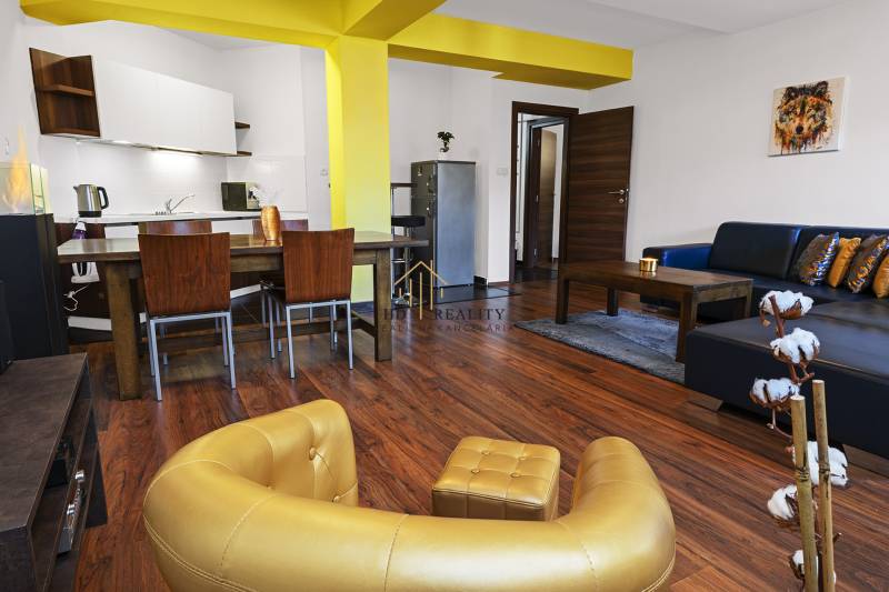 Living room in a two-room apartment with a sofa, kitchenette, and dining table.