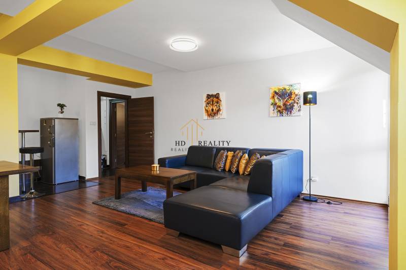 A living room in a 2-room apartment with a dark couch, wooden floor, and a striking yellow wall.
