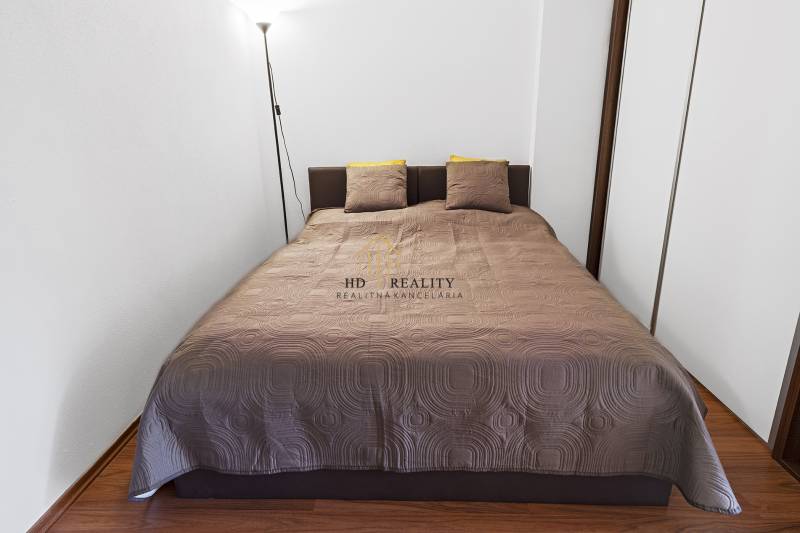 Bedroom with a double bed and a lamp in a 2-room apartment, simple design, wooden floor.