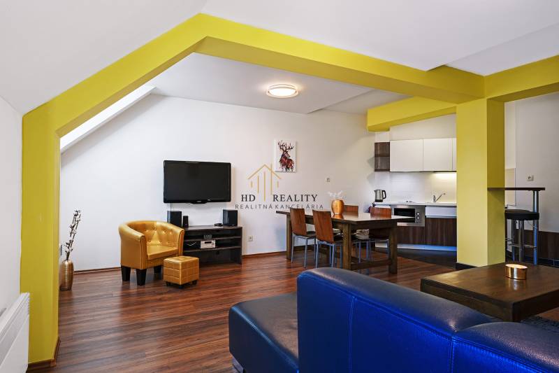 Living room in a two-room apartment with wooden flooring, a yellow wall, and a television.