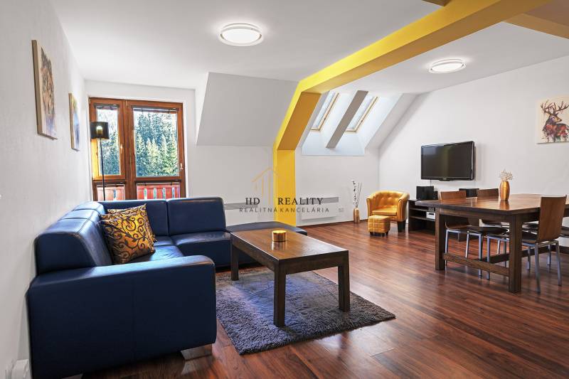 Living room in a two-room apartment with a blue sofa, wooden table, and television.
