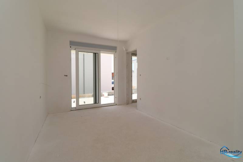A bright room in a recreational apartment with a large window and an unfinished floor.