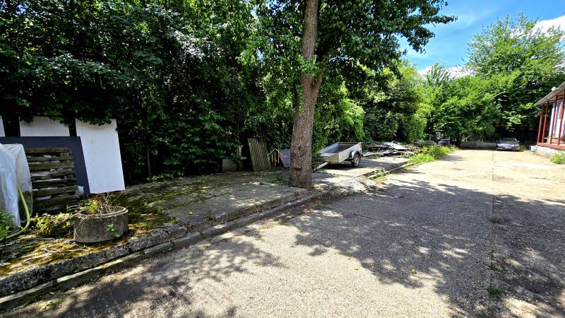 A trailer and car area among trees around warehouses and halls of Banská Bystrica.
