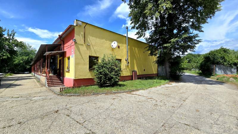 A yellow building with metal stairs, next to it trees, surrounded by greenery in warehouses and halls.