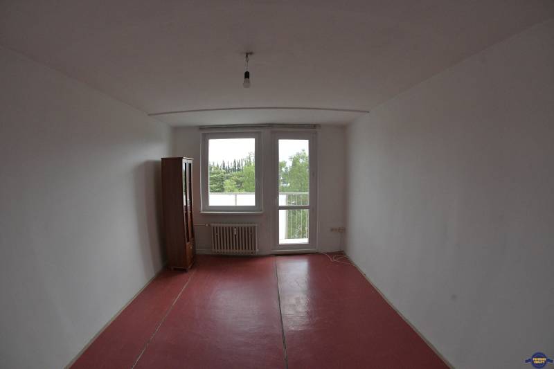 A room with a red floor and a wardrobe in a 2-room apartment, view of greenery.