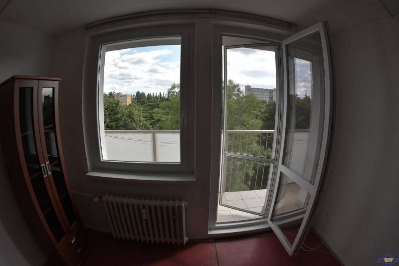 Interior of a 2-room apartment with a view of trees and buildings through an open window and balcony.