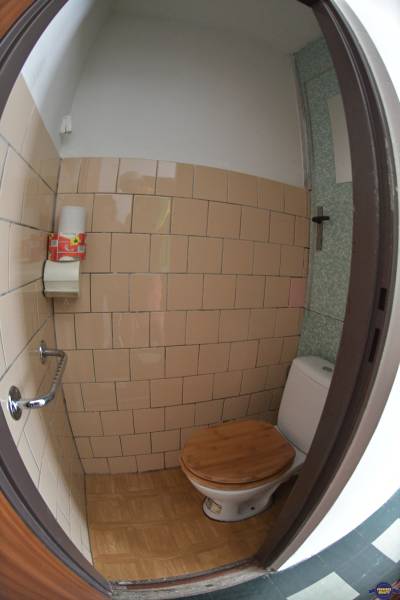 A toilet in a 2-room apartment with a wooden seat and beige tiles.