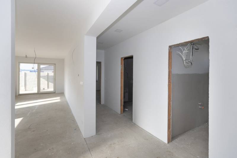 A hallway in a family house with empty rooms and a large window at the end.