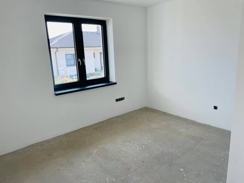 An unfurnished room in a family house with a window, overlooking the neighboring house.