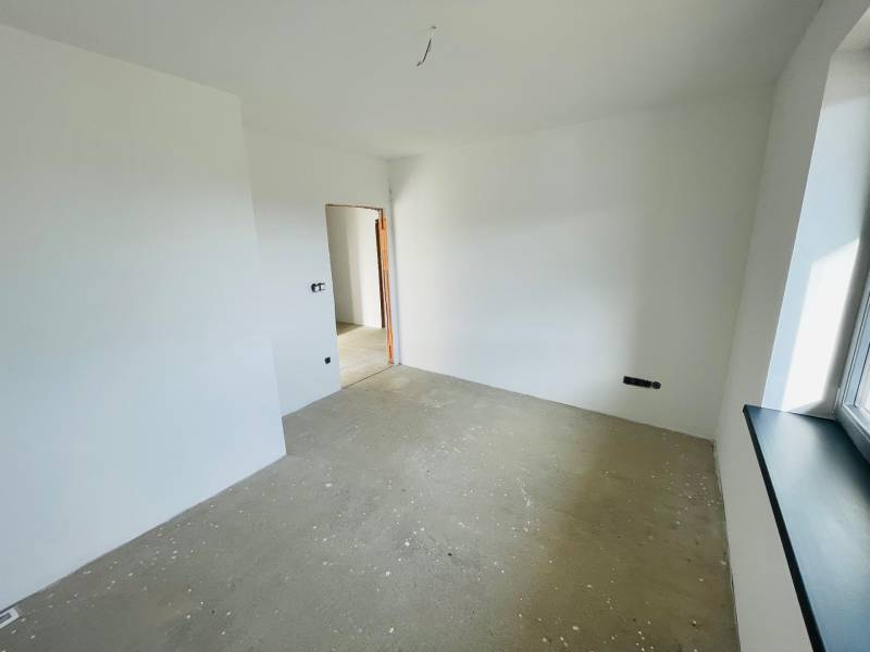 An empty room with white walls and a concrete floor in a family house.
